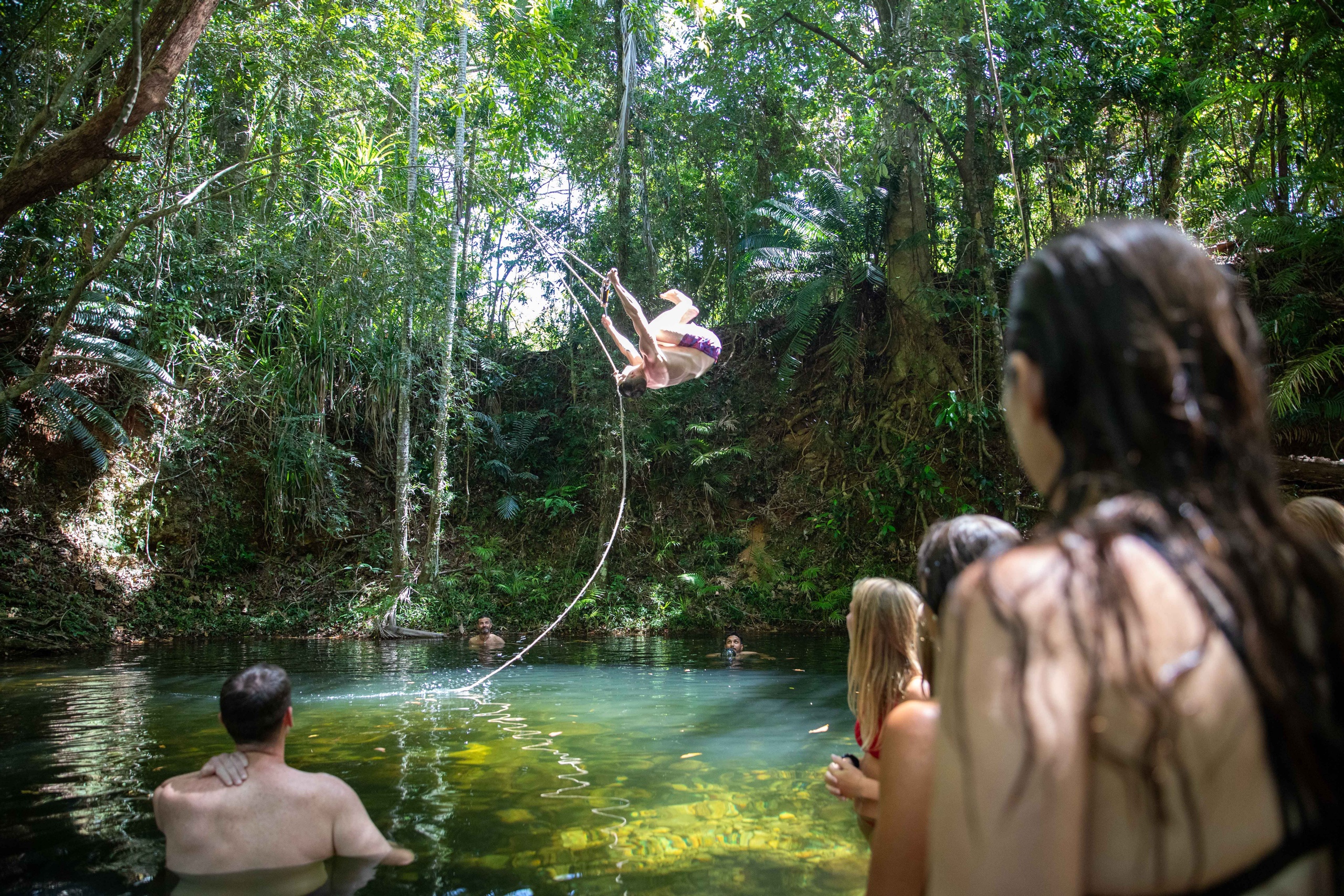 Adventurer swings on a rope over a lush forest pond during the renowned 1 Day Cape Tribbbin Tour With Uncle Brian in Queensland.