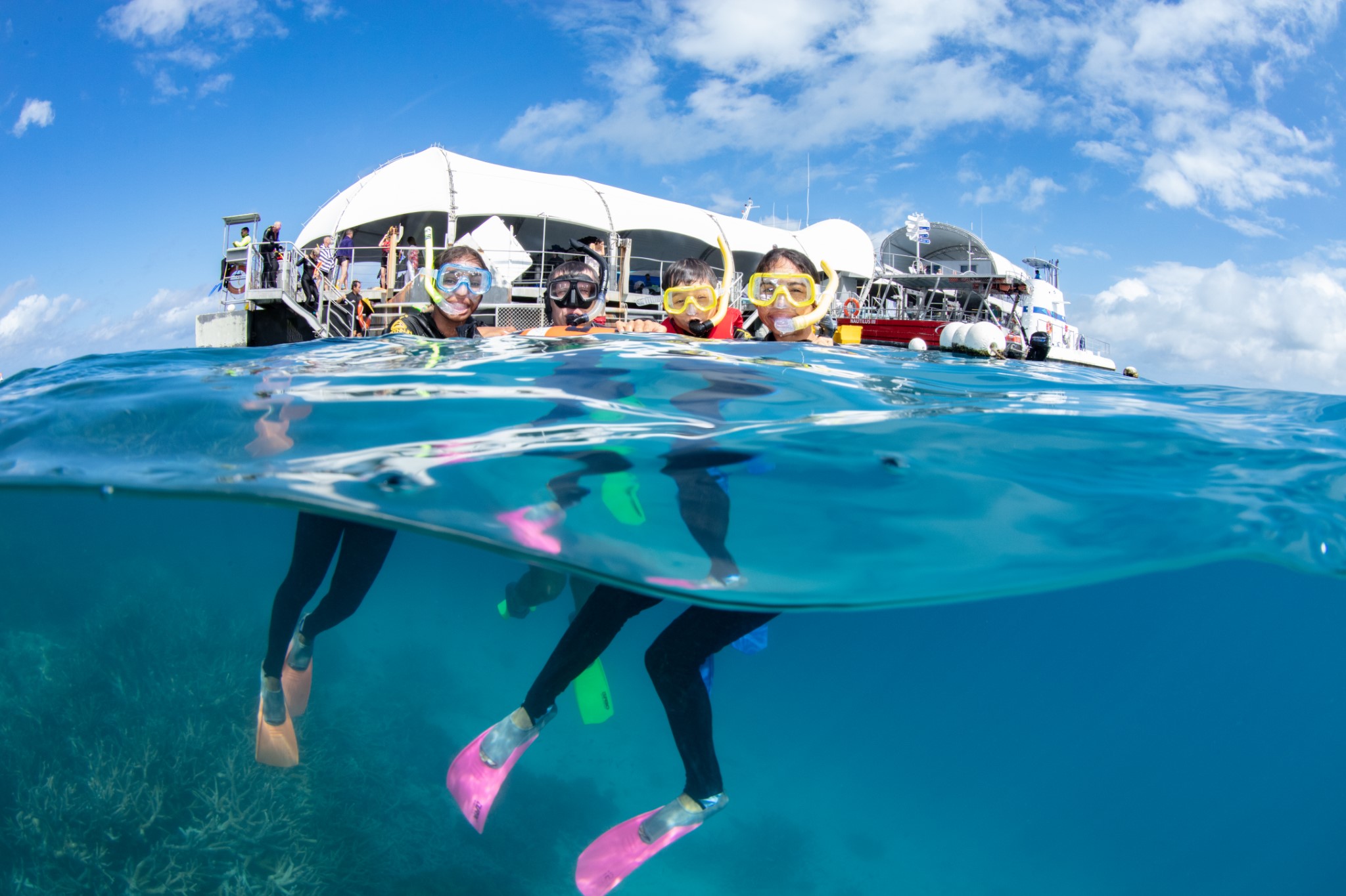 Snorkellers explore crystal-clear blue waters beside the Green Island Outer Barrier Reef Activity Platform under a bright, sunny sky.