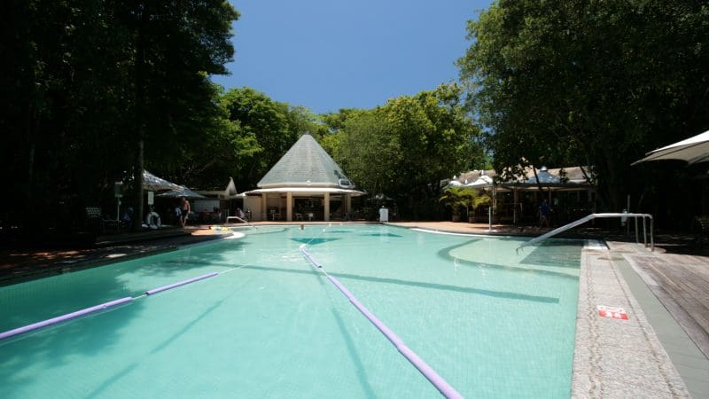 Relax by a sparkling outdoor swimming pool with colourful pool noodles, shaded by trees and a pavilion—perfect before Green Island Transfers.
