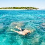 Two snorkellers and a glass-bottomed boat at Green Island above vibrant coral reef, gliding over crystal-clear blue waters in Cairns, Australia.