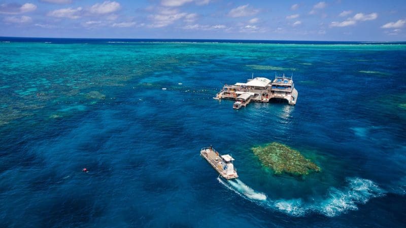 Experience a boat arriving at the Quicksilver Outer Barrier Reef Platform atop crystal-clear blue waters and colourful tropical coral reefs.