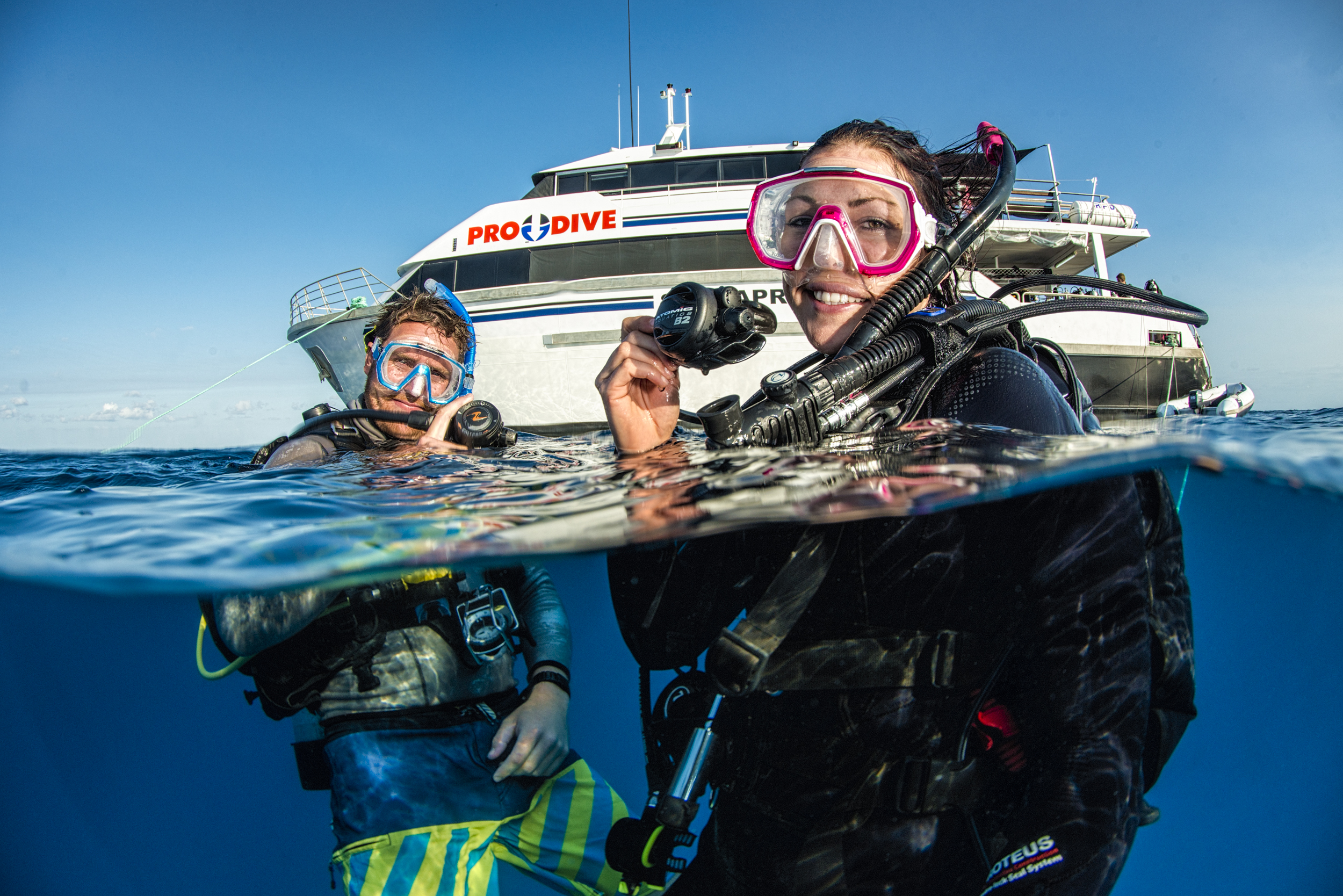 Two scuba divers happily surface after completing a 5-Day PADI Open Water Course with Pro Dive Cairns, enjoying their achievement.