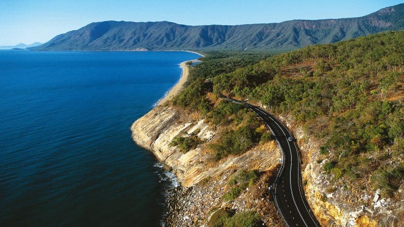 Scenic coastal road ideal for a Private Exclusive Daintree Mossman Tour, winding beside the ocean under a vibrant blue sky.
