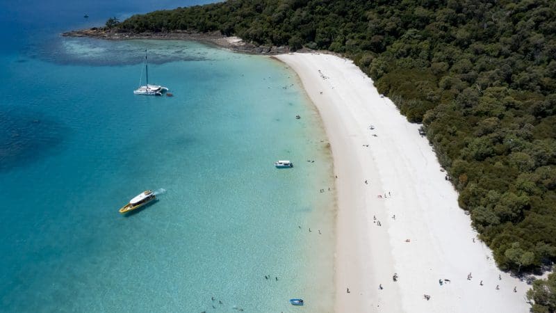 Stunning aerial view of Whitehaven Beach’s turquoise waters, boats, swimmers, and lush forest—top spot for snorkelling enthusiasts.