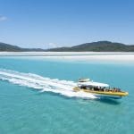 Yellow speedboat glides by Whitehaven Beach, lush Whitsunday hills and top Coral Reef snorkelling sites visible in turquoise waters.