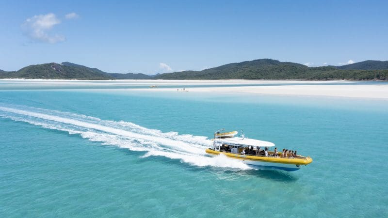 Yellow speedboat glides by Whitehaven Beach, lush Whitsunday hills and top Coral Reef snorkelling sites visible in turquoise waters.