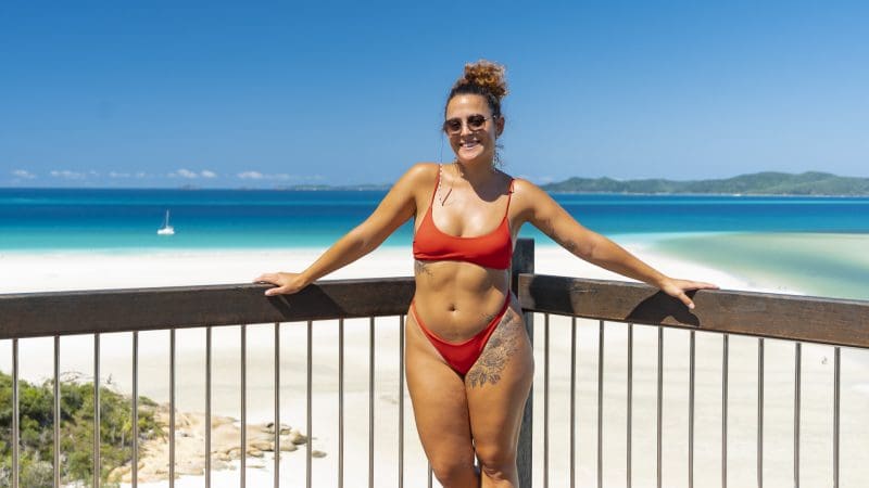 Woman in red bikini stands on deck, admiring Big Fury Whitsundays’ stunning Whitehaven Beach and crystal-clear coral reef waters.