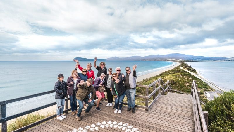 Tourists enthusiastically wave from a scenic lookout deck on the Bruny Island Food Sightseeing & Cape Bruny Lighthouse Tour experience.
