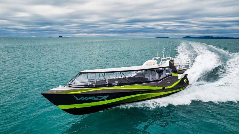 VIPER, a striking black and green speedboat, powers through the Outer Great Barrier Reef Tour beneath dramatic cloudy skies.
