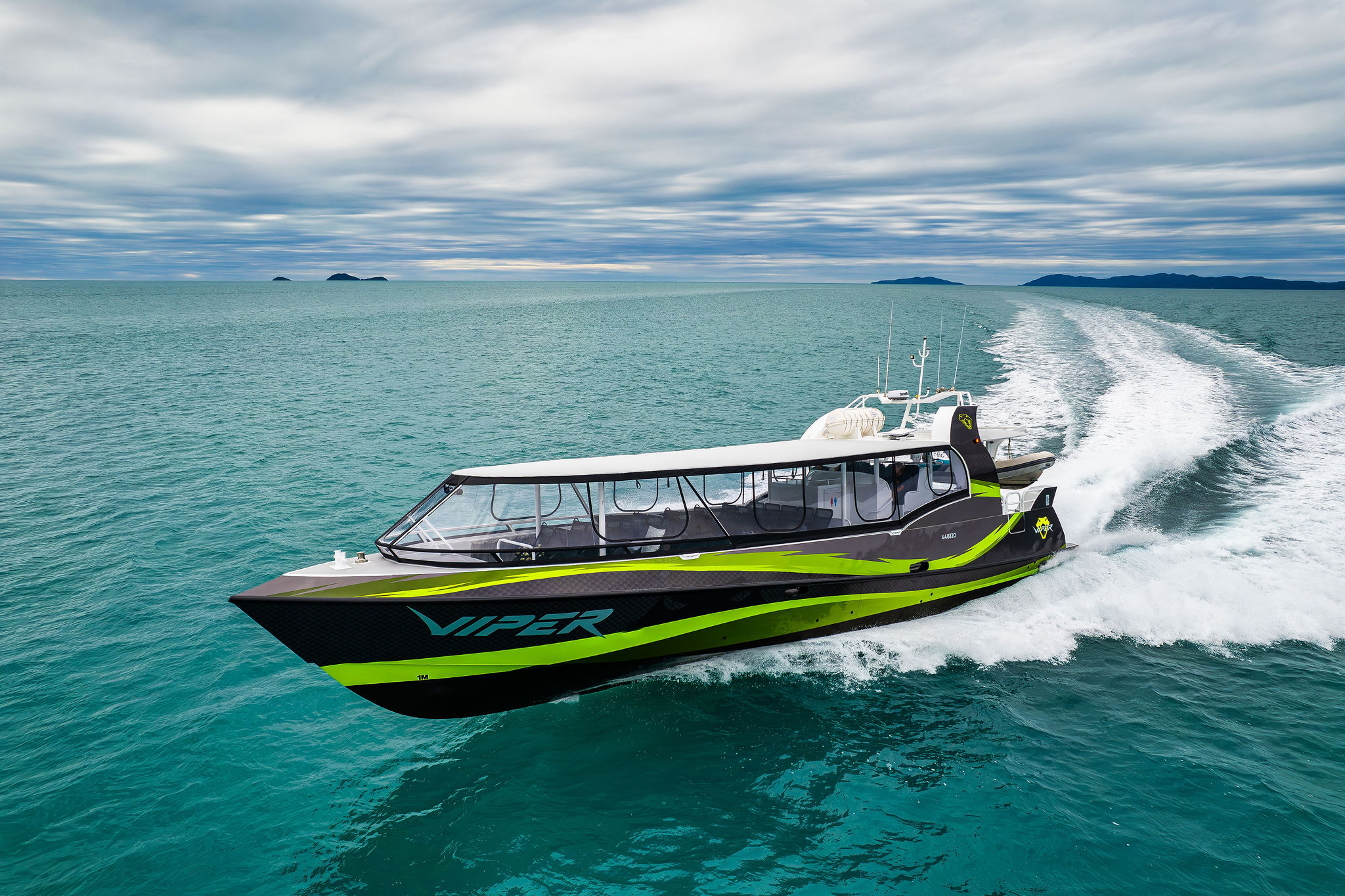 VIPER, a striking black and green speedboat, powers through the Outer Great Barrier Reef Tour beneath dramatic cloudy skies.