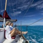Two people unwind on Lady Enid yacht under sunny skies, overlooking turquoise waters near Whitehaven Beach after a snorkelling adventure.