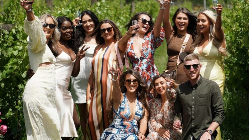 Smiling friends toast together outdoors under sunny skies during a Yarra Valley winery tour, enjoying a relaxed group experience.