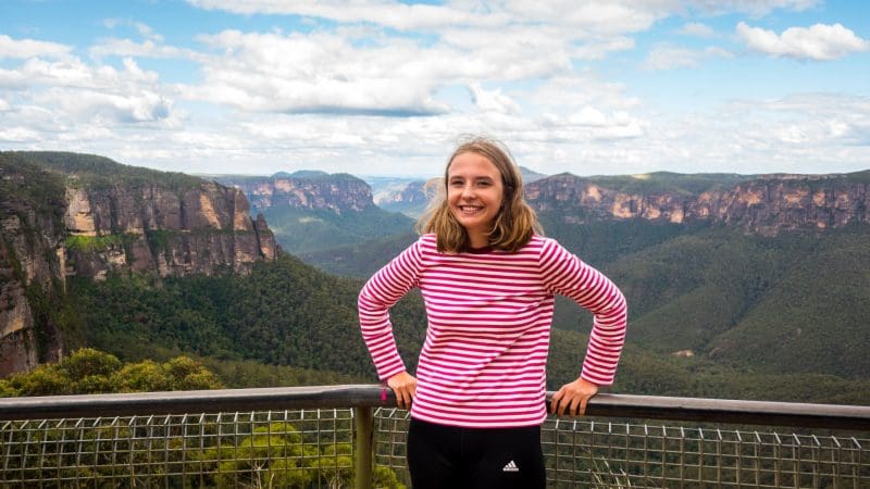 Happy woman in a red striped top admires scenic Blue Mountains views on exclusive 1 Day Wildlife Park Trip, perfect for travel seekers.