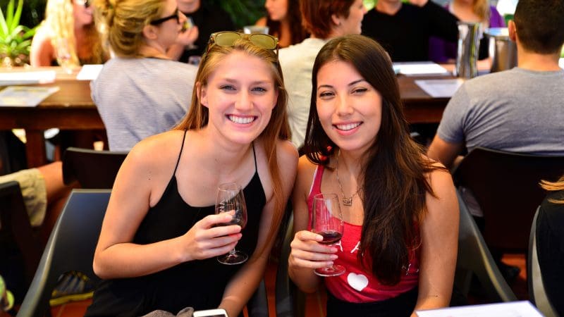 Two women savour red wine outdoors on a 1 Day Hunter Valley Wineries Tour from Sydney with Colourful Collective Travel, scenic vineyard views.