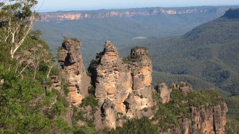 The Three Sisters—iconic sandstone pillars—tower over a lush forested valley in the Blue Mountains All-Inclusive Day Tour.