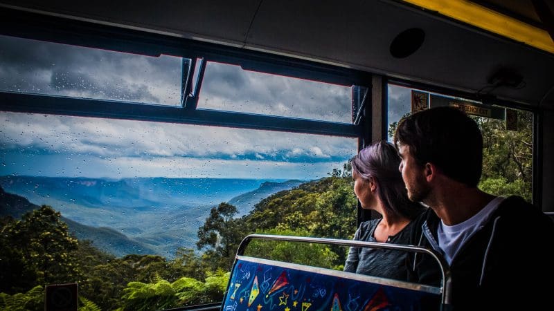 Scenic Boomerang Pass coach tour: two travellers enjoy panoramic views of misty mountain peaks on a one-hour sightseeing adventure.