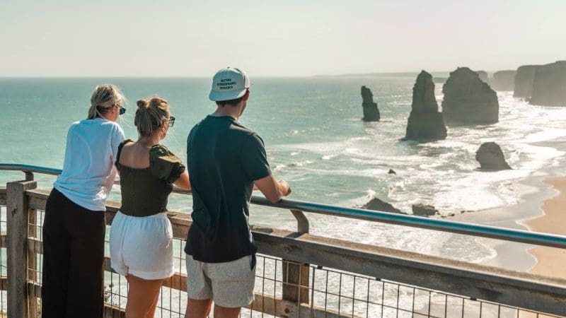 Three travellers on a wooden lookout admire stunning sea stacks, capturing the essence of Melbourne’s top coastal adventure experience.