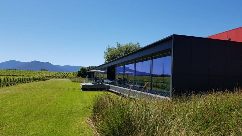Contemporary winery with expansive glass windows offers panoramic views over lush Yarra Valley vineyards, ideal for top wine tasting.