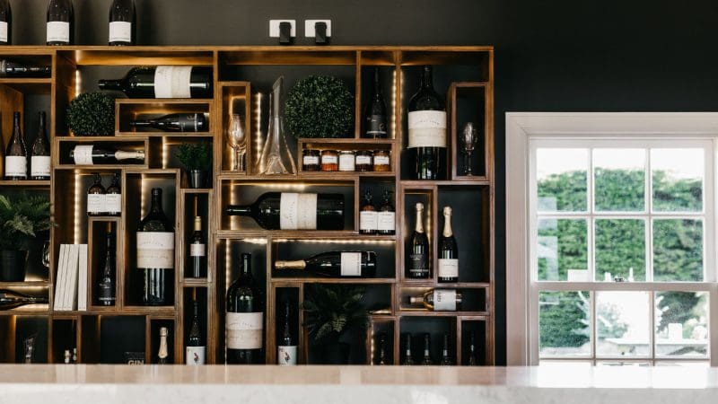 Sunlit wooden shelves showcase premium wine bottles and crystal glasses, creating an inviting gourmet wine tasting lunch atmosphere.