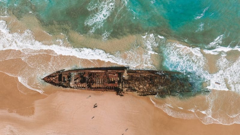 Stunning aerial shot of a rusted shipwreck on pristine sandy beach, ocean waves lapping—ideal for Kgari 3 Day Getaway adventure.