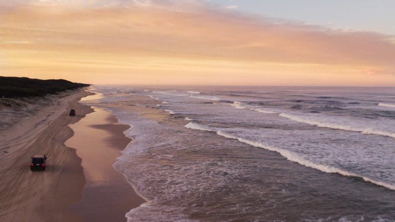 4WD vehicle cruising along Fraser Island’s sandy beach at sunset during an Island Expeditions Kgari Tours camping adventure.