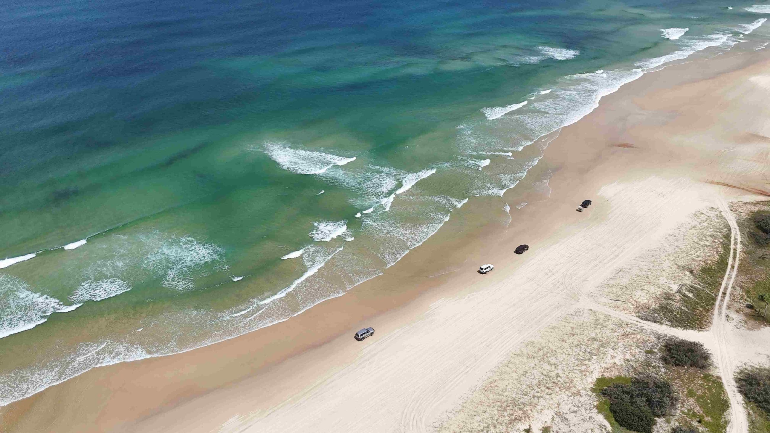 Aerial view of 4WD vehicles driving along pristine sandy beach—perfect for Fraser Island Tag Along Tours from Noosa or Rainbow Beach.