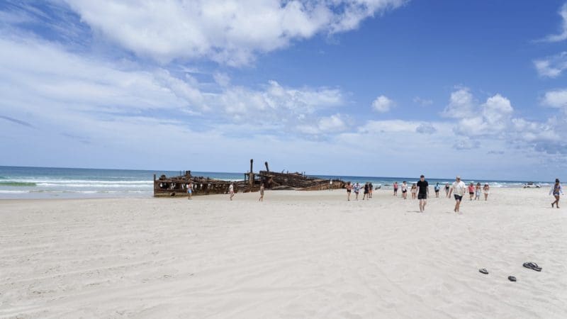 Visitors explore a scenic sandy beach, approaching a famous shipwreck on Fraser Island during the top-rated K'gari Safari 4WD tour.