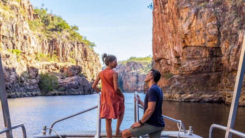 Couple on a 1 Day Katherine Gorge Cruise, gliding through dramatic red cliffs and tranquil waters beneath a vibrant blue sky.