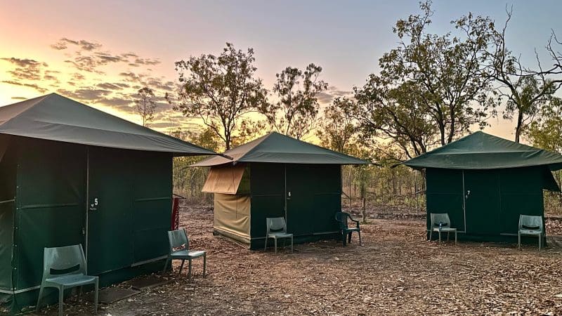 Three green tents and camping chairs on dry earth at sunset during a Kakadu Litchfield Tour—iconic outback adventure camping scene.
