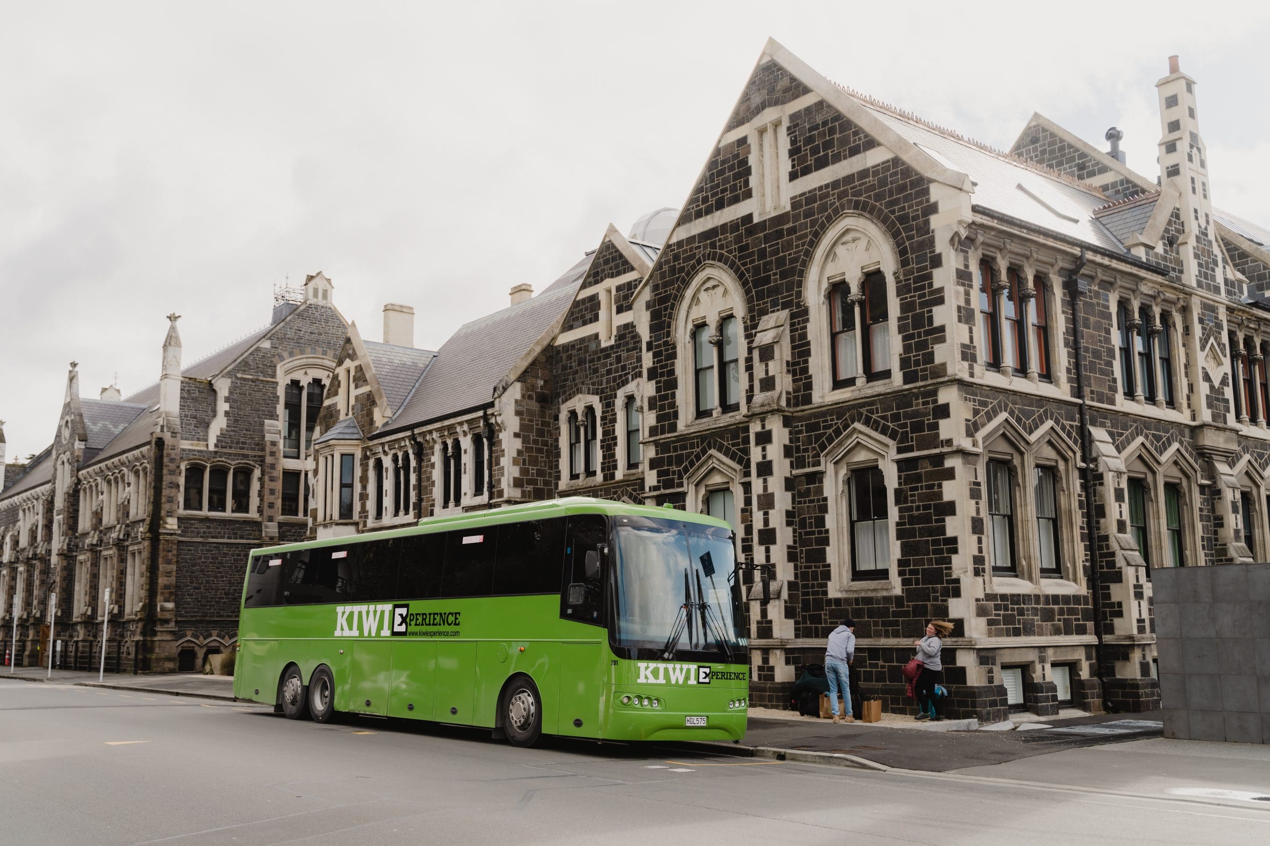 Vibrant green bus parked roadside beside a historic stone building, ideal urban transport near architecture, city street scene.