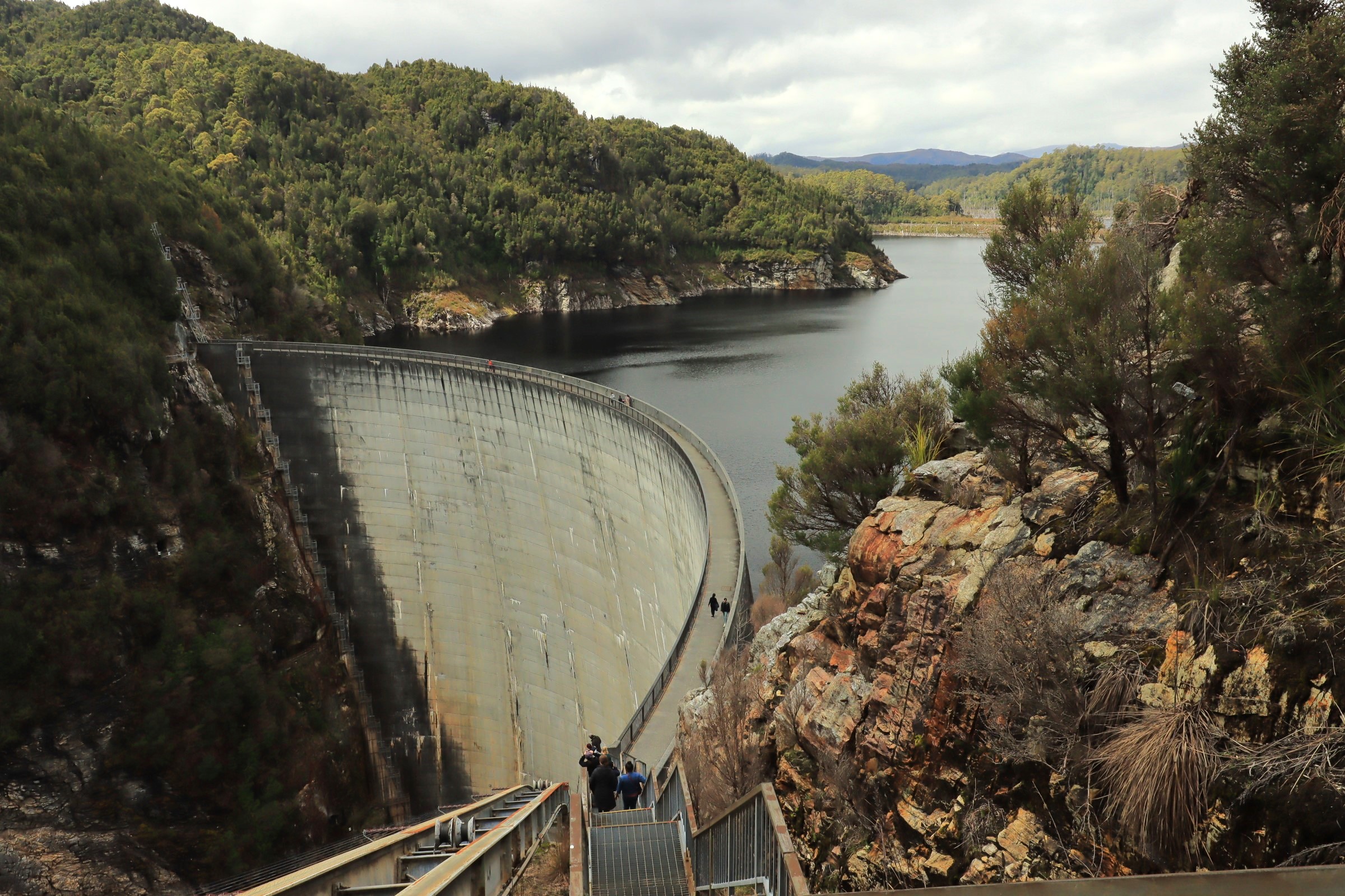 Visitors descend stairs towards the iconic Gordon Dam in Lake Pedder Wilderness on a guided small group tour beneath overcast skies.