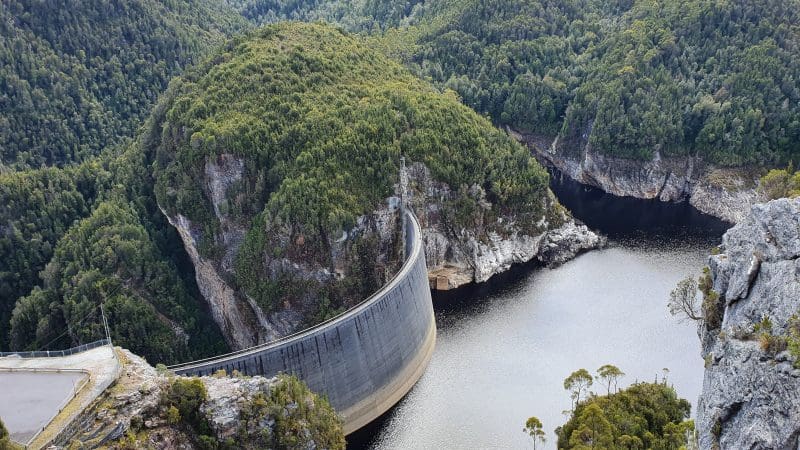The impressive curved Gordon Dam stretches across tranquil waters, surrounded by lush forested hills on the Lake Pedder Wilderness tour.