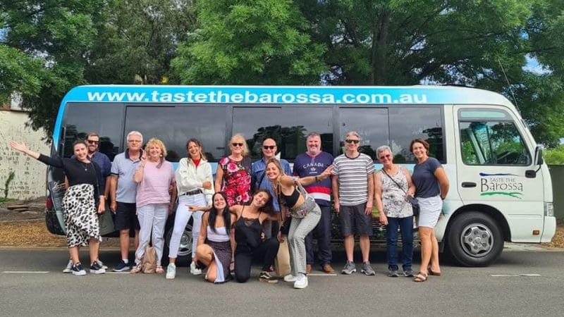 Happy group posing in front of Taste The Barossa Premium Wine Tour coach, parked on a scenic street for a memorable South Australia wine tour.