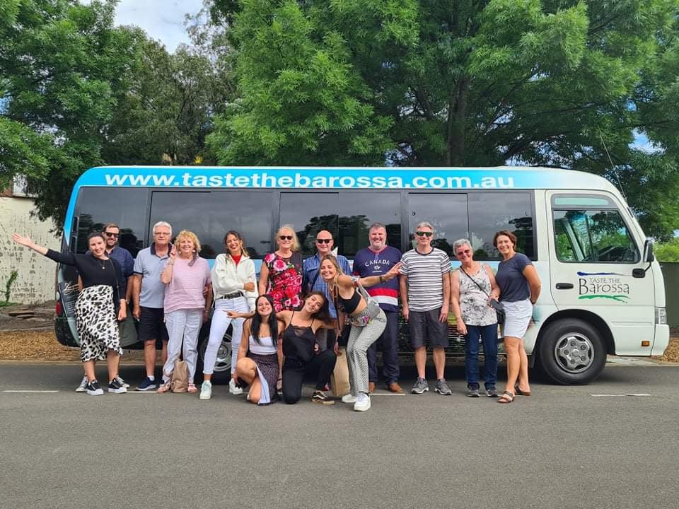 Happy group posing in front of Taste The Barossa Premium Wine Tour coach, parked on a scenic street for a memorable South Australia wine tour.