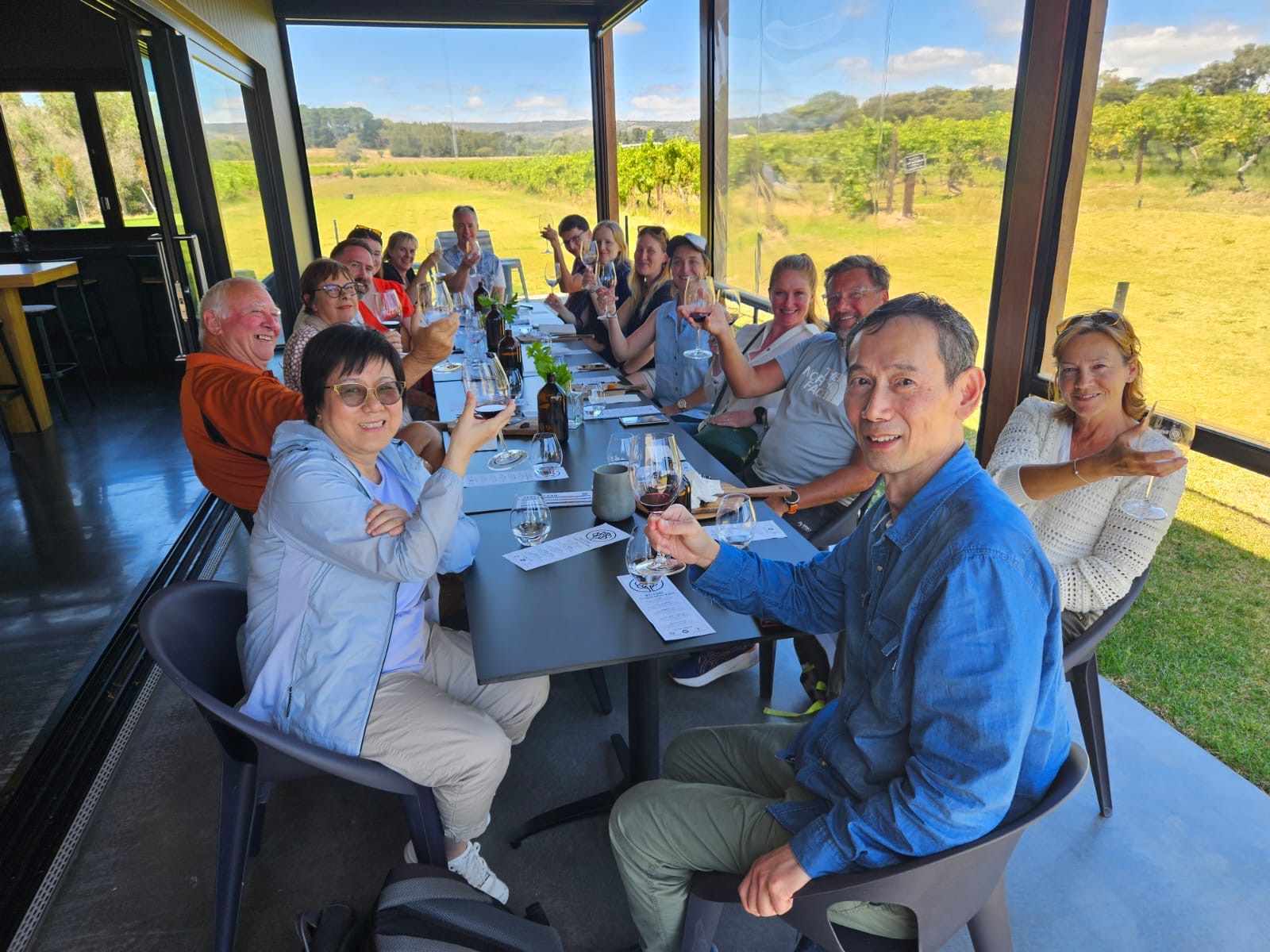 Happy group toasting with wine at a bright outdoor Adelaide restaurant, enjoying the Highlights and Coast Full Day Wine Tasting tour.