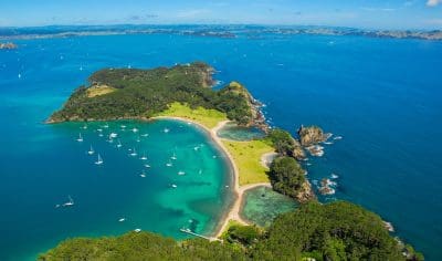 Stunning aerial view of Bay of Islands’ lush green island, pristine sandy beaches, turquoise waters, yachts by Hole in the Rock.