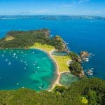 Stunning aerial view of Bay of Islands, featuring vibrant lush greenery, sailboats on crystal-clear turquoise waters, and pristine sandy beach.