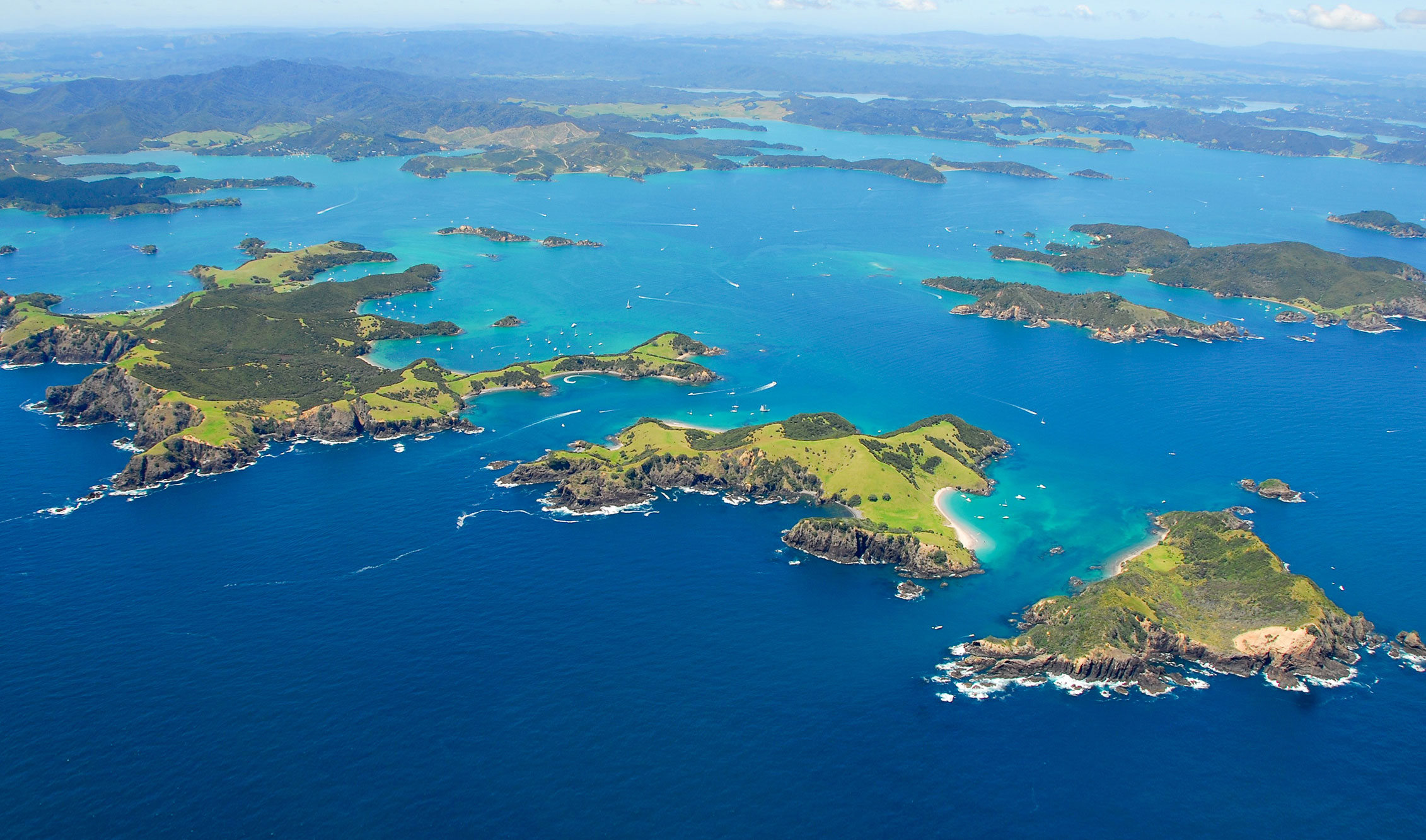 Stunning aerial view of Bay of Islands’ lush green islands and turquoise waters, boats cruising near the iconic Hole in the Rock.