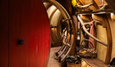 Step through a round red door into a charming Hobbiton Movie Set hallway, a must-see highlight for unforgettable movie set tours.