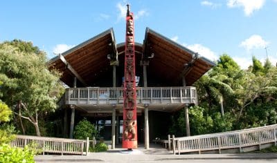 Contemporary West Coast building featuring a striking wooden roof, prominent red totem pole, and lush landscaped greenery at the entrance.