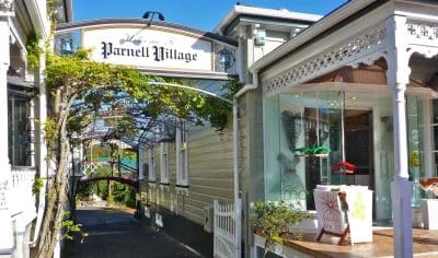 Parnell Village entrance in Auckland City showcasing historic white buildings, arched gateway, lush greenery, and vibrant blue sky.