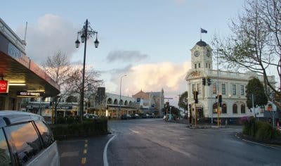 Auckland city street at sunset with shops, iconic white clock tower, wet pavement reflecting lights, serene urban evening landscape.