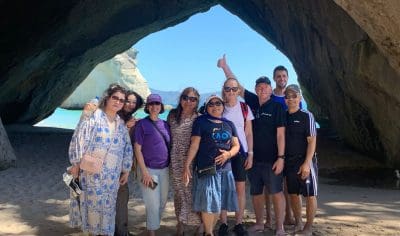 Tourists smile and pose together in a dramatic rocky cave on Coromandel’s sunlit coast, highlighting a top-rated New Zealand beach tour.