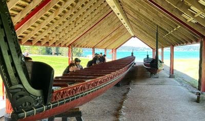 Tourists admire two impressive wooden Viking ships beneath an open waterfront shelter, highlighting Norse maritime history.