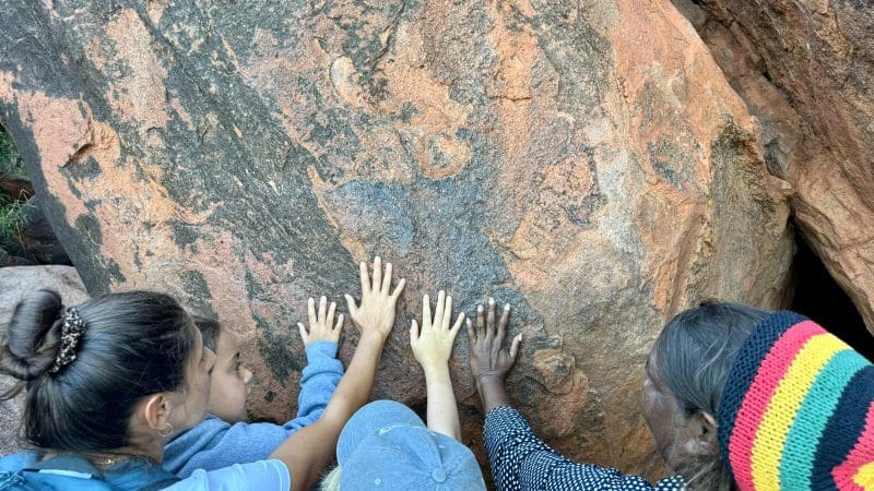 A group of four, guided by an elder in a vibrant hat, explore ancient Aboriginal art on the 7 Day Uluru to Adelaide Untamed Escapes tour.