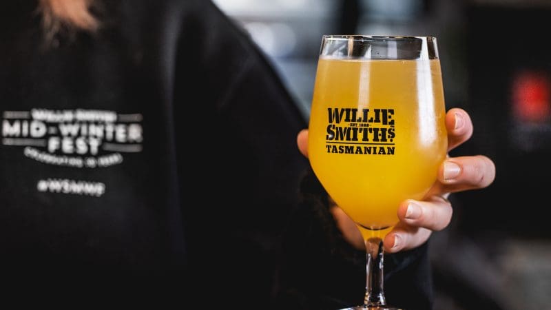 A hand holds a glass of Willie Smiths Tasmanian cider, yellow in colour, on a Huon Valley Safaris Private Day Tour in Tasmania.