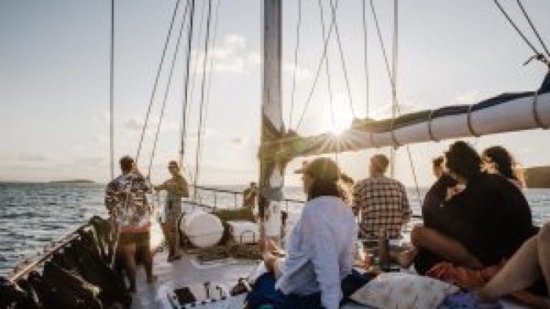 a group of people on the bow of summer jo at sunset