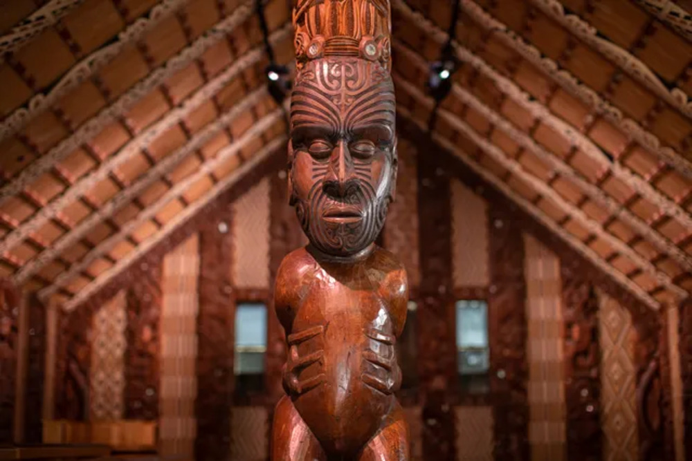 Intricately tattooed wooden Māori carving in a traditional meeting house at Waitangi Treaty Grounds, historic site in New Zealand.