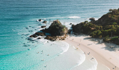 Stunning aerial shot of a sunlit sandy beach with surfers riding waves, ideal for The Great Escape Australia 28 Day Semi-Guided adventure.