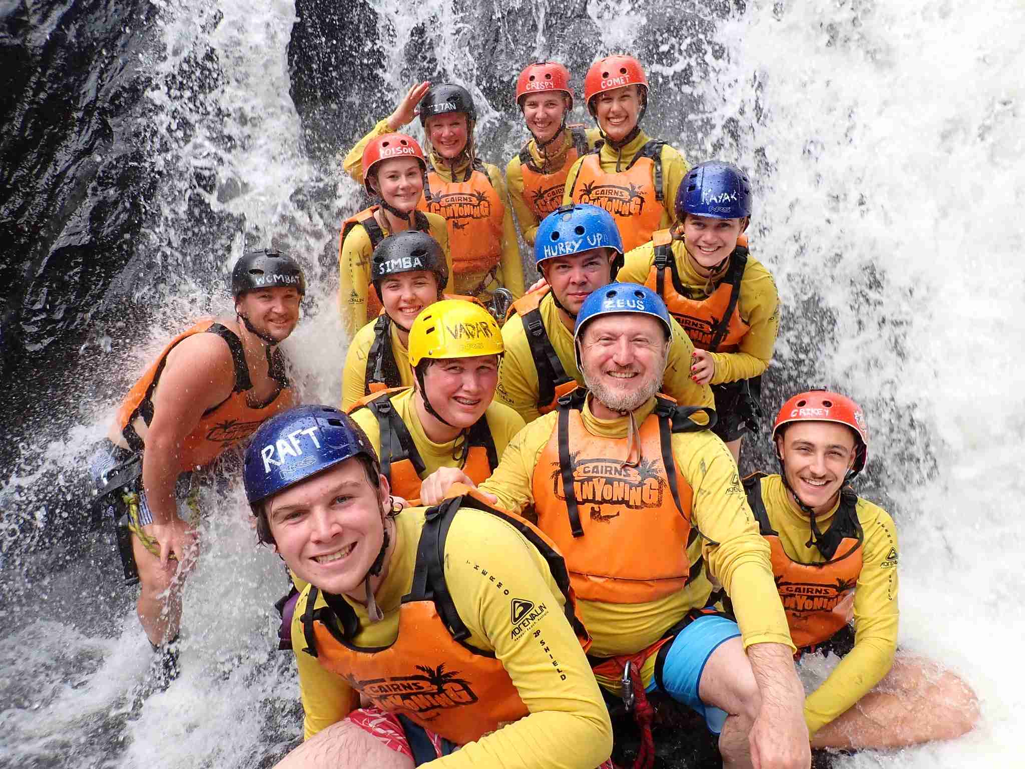 Smiling adventurers in helmets and life jackets pose by picturesque Crystal Cascades waterfall during an unforgettable canyoneering tour.